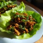 Close-up of savory chicken lettuce wraps filling served in a crisp butter lettuce cup, garnished with green onions.