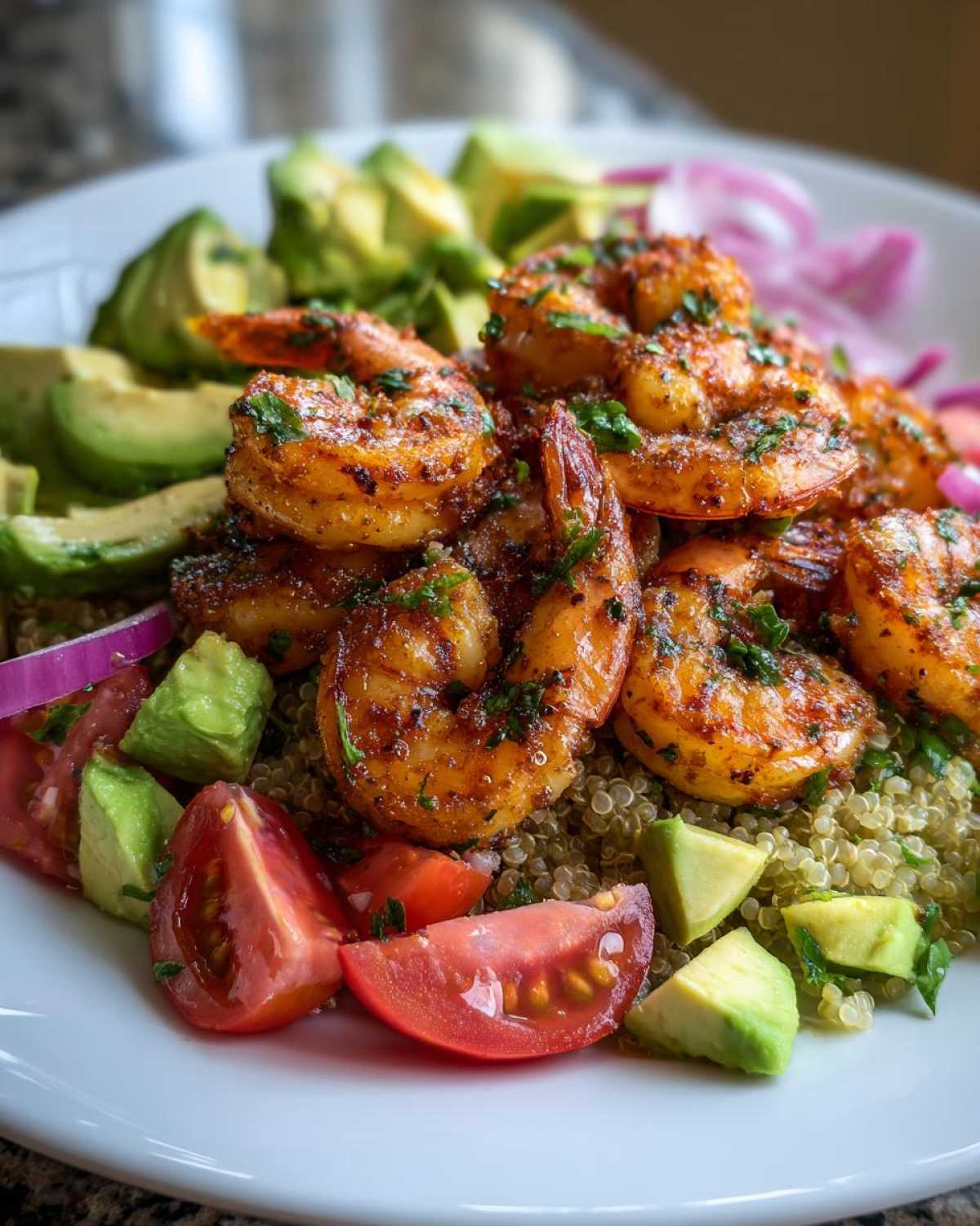 A close-up of a vibrant shrimp and avocado bowls featuring seasoned shrimp over quinoa with diced tomatoes and avocado.
