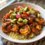 A close-up of a delicious shrimp and avocado bowls featuring seasoned shrimp over quinoa, topped with diced avocado, tomatoes, and red onion.