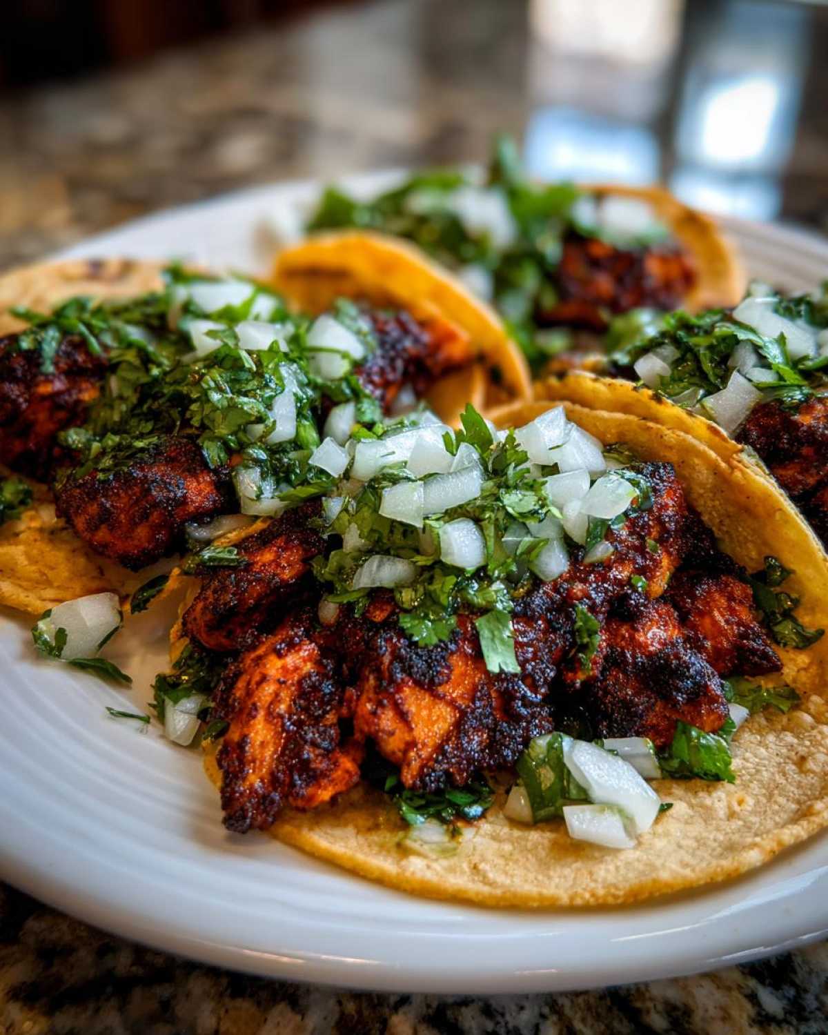 Close-up of several smash chicken tacos filled with charred chicken, diced white onion, and fresh cilantro on a white plate.
