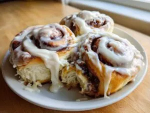 Close-up of three fluffy sourdough discard cinnamon rolls generously topped with white icing, served on a white plate.