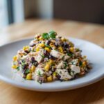 A mound of creamy southwestern chicken salad featuring chunks of chicken, black beans, and corn, garnished with parsley.