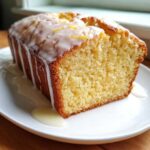 A close-up of a slice of Starbucks copycat lemon loaf, showing the moist crumb and thick white lemon glaze dripping down the side.