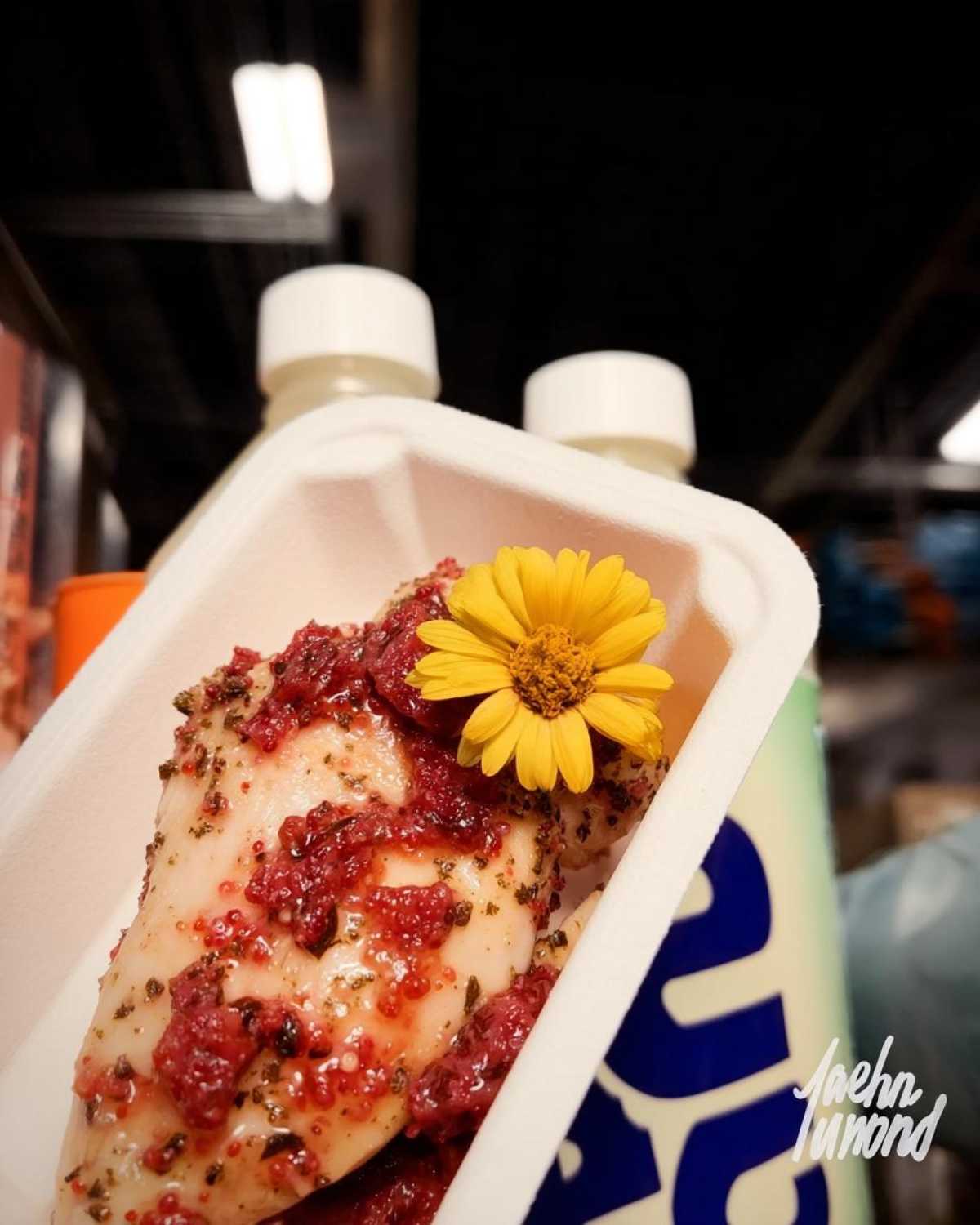 Close-up of a seasoned strawberry basil chicken breast topped with a bright yellow edible flower in a white container.