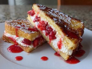 Two halves of strawberry cheesecake stuffed french toast stacked, filled with cream and strawberries, drizzled with sauce.