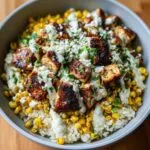 A close-up of a street corn chicken bowl featuring seasoned chicken, corn, rice, creamy sauce, and crumbled cheese.