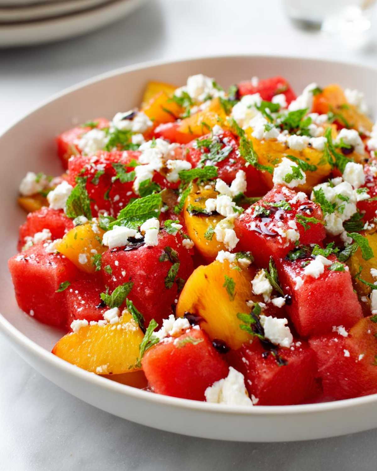 Close-up of a refreshing summer peach watermelon salad topped with feta cheese, mint, and balsamic glaze.