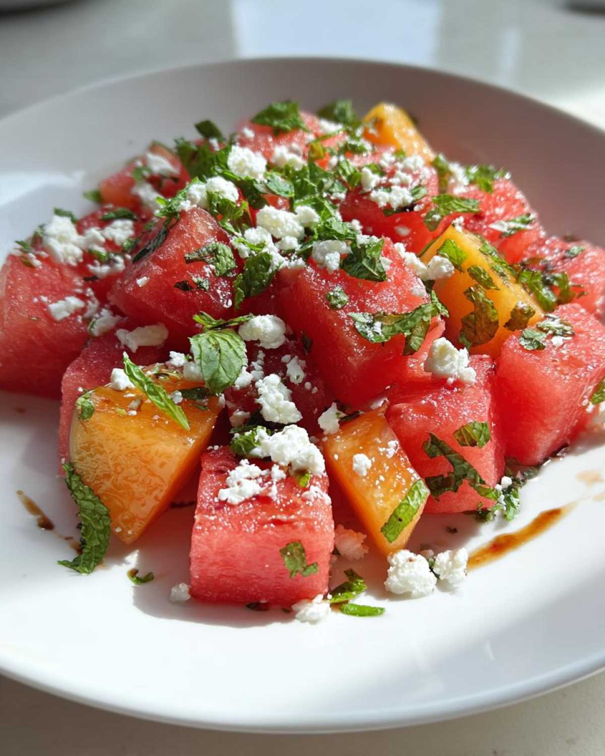 Close-up of a vibrant summer peach watermelon salad topped with crumbled feta cheese and fresh mint.