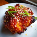 Close-up of a piece of glazed sweet chili chicken topped with sesame seeds and sliced green onions.