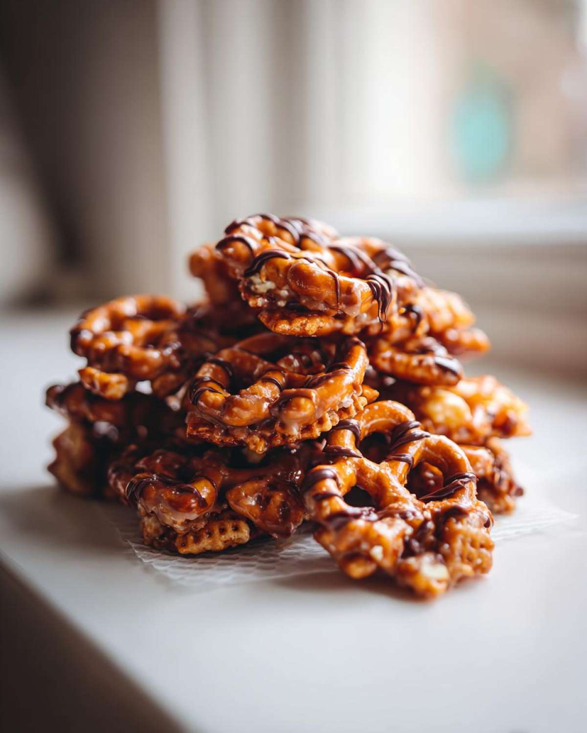 A pile of homemade toffee chex mix recipe pieces, featuring pretzels coated in sticky toffee and drizzled with dark chocolate.