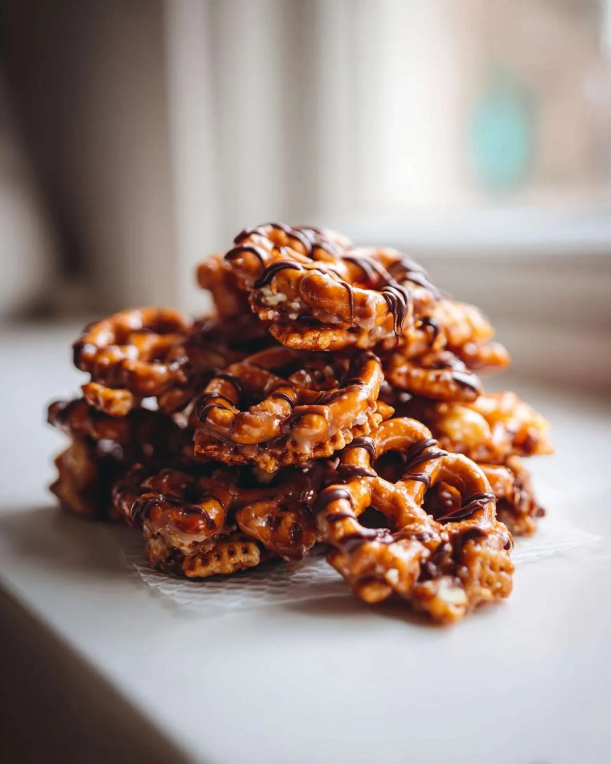 A pile of homemade toffee chex mix recipe pieces, featuring pretzels coated in sticky toffee and drizzled with dark chocolate.
