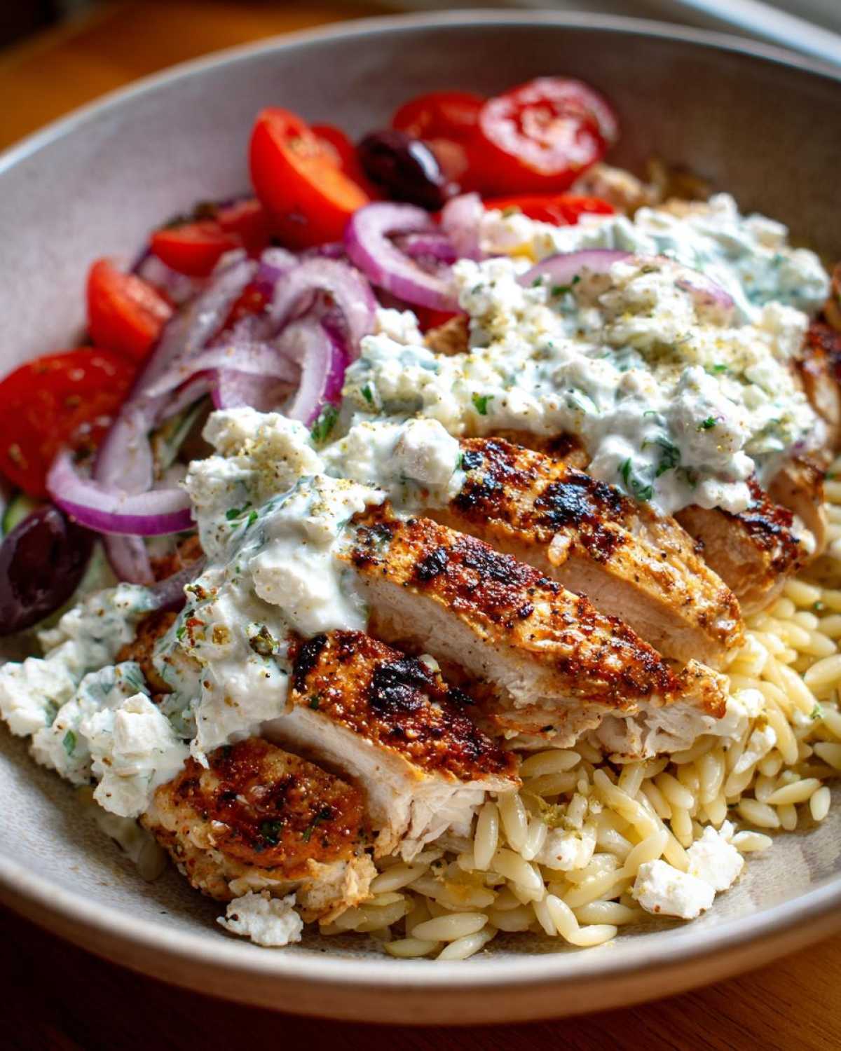 Close-up of sliced, seasoned chicken breast topped with tzatziki sauce in one of the ultimate chicken tzatziki bowls, served over orzo.