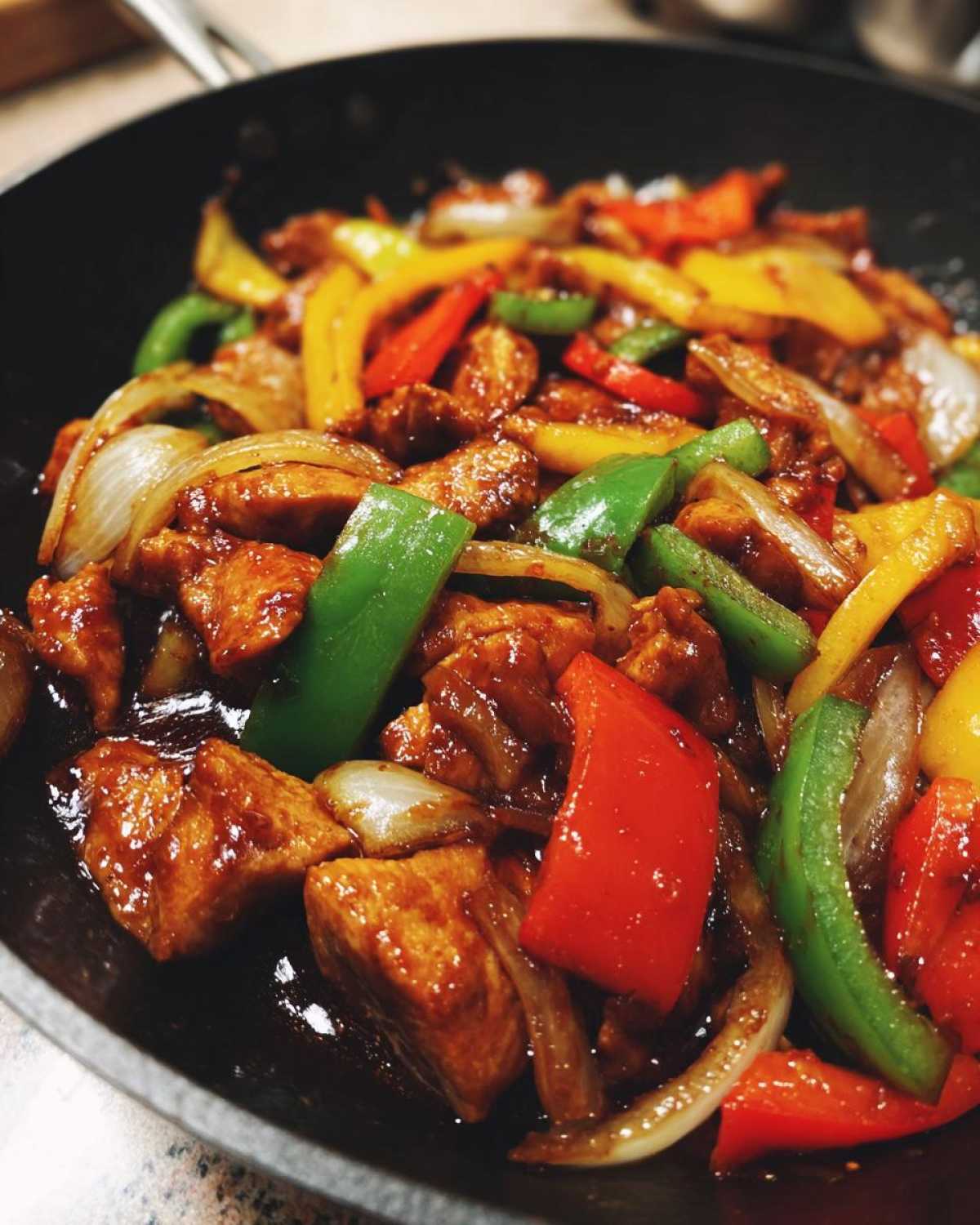 Close-up of colorful pepper chicken stir fry with red, green, and yellow peppers and onions coated in a glossy sauce.