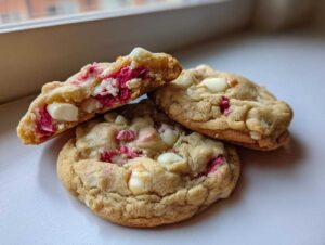 Three delicious white chocolate raspberry cookies stacked, with one broken open showing the soft interior and bright pink raspberry pieces.