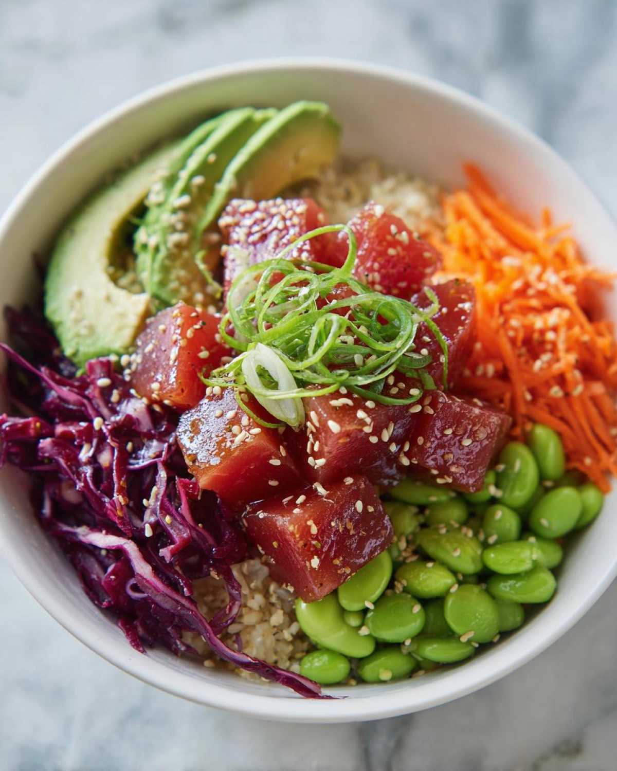 Close-up of a vibrant Ahi tuna poke bowl featuring marinated tuna cubes, avocado slices, edamame, shredded carrots, and red cabbage.