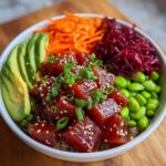 Close-up of a colorful Ahi tuna poke bowl featuring marinated tuna, avocado, edamame, carrots, and beets.