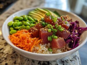 A vibrant Ahi tuna poke bowl featuring marinated tuna cubes, brown rice, edamame, shredded carrots, red cabbage, and avocado slices.