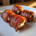 Close-up of four perfectly cooked bacon wrapped dates with goat cheese filling on a white plate.