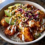 A close-up of a delicious baja fish taco bowls featuring crispy fish pieces over rice, topped with slaw, avocado, and white sauce.