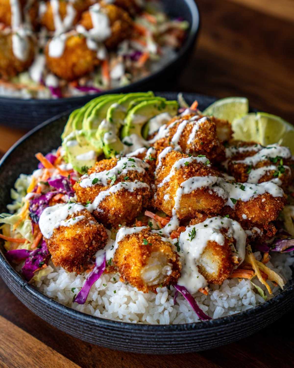 Close-up of a Baja fish taco bowls featuring crispy fried fish pieces over rice, slaw, avocado, and drizzled with white sauce.