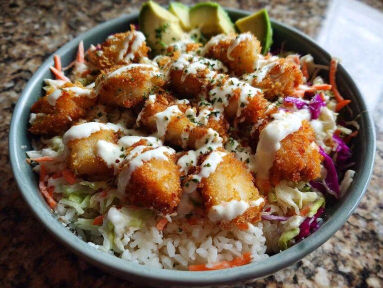A close-up of a serving of Baja fish taco bowls featuring crispy fried fish pieces, white rice, slaw, and a drizzle of white sauce.