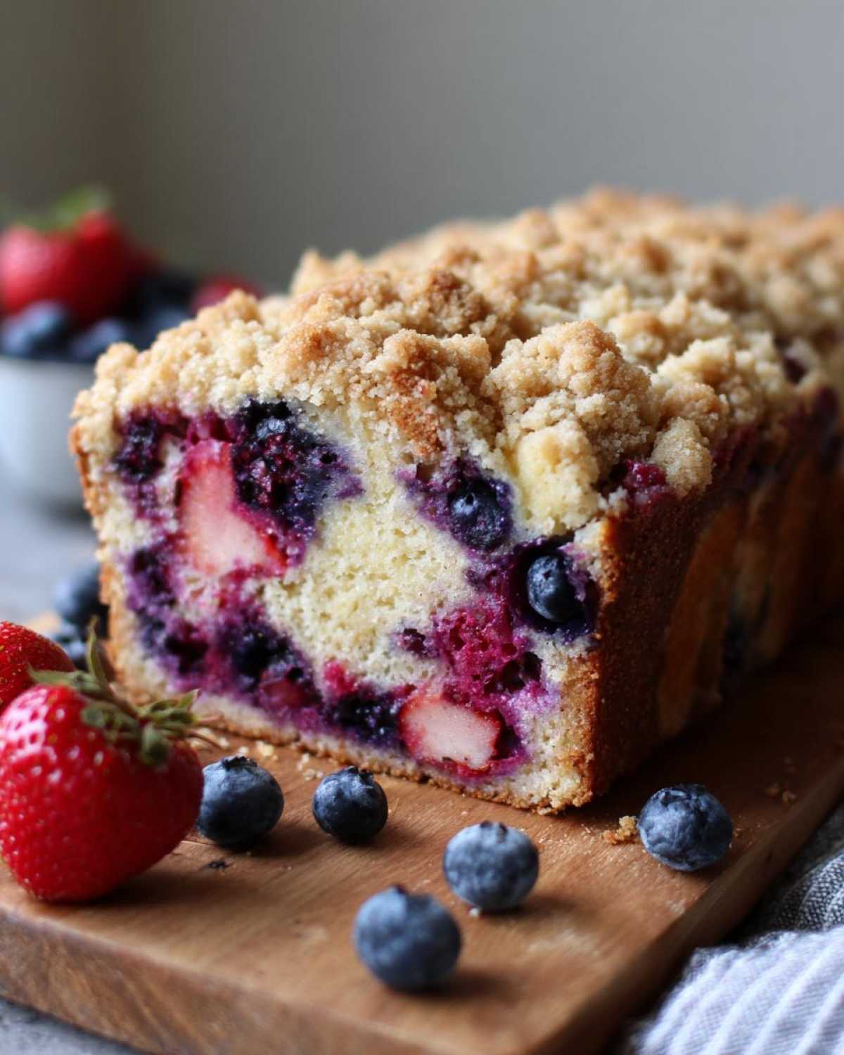 A loaf of Berry French toast bake featuring visible strawberries and blueberries, topped with a golden crumb topping.