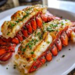 Close-up of two perfectly cooked broiled lobster tail halves, split and topped with butter and fresh parsley.