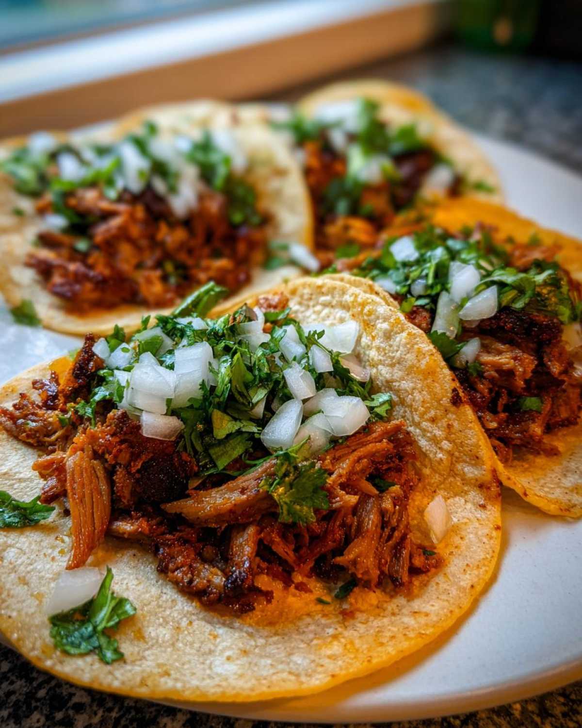 Close-up of several Tacos árabes served on corn tortillas, filled with seasoned meat and topped with diced white onion and cilantro.