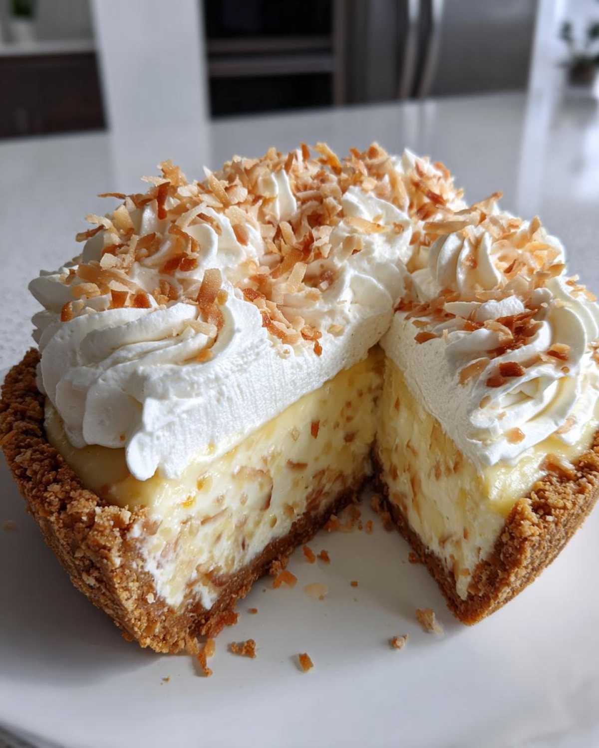 Cross-section view of a rich Coconut cream pie with a thick graham cracker crust, creamy filling, and whipped topping sprinkled with toasted coconut.