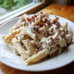 A close-up of penne pasta coated in a rich, white sauce with chicken pieces and topped with crumbled bacon, representing Creamy Chicken Bacon Ranch Pasta.