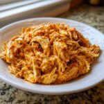 A close-up of shredded chicken coated in a rich, orange-red sauce, representing the creamy crockpot cajun butter chicken.