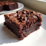 A close-up, fudgy cottage cheese brownies square topped with melted chocolate chips, sitting on a white plate.