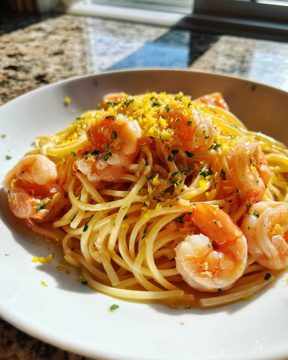 A close-up of Garlic butter shrimp scampi served over spaghetti, topped with bright yellow lemon zest and parsley.