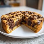A round Chocolate chip cookie cake with a slice removed, showing a gooey, melted chocolate center.