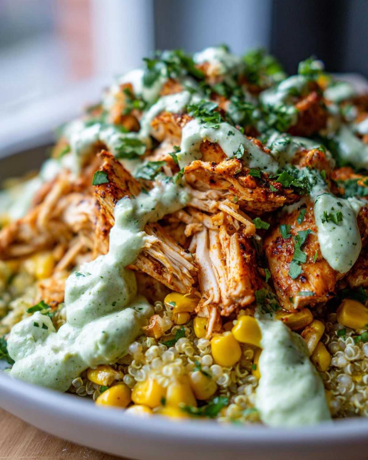 Close-up of a healthy street corn chicken bowl featuring shredded spiced chicken, corn, quinoa, and a creamy green sauce.
