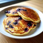 Close-up of three fluffy Lemon blueberry cottage cheese pancakes stacked on a white plate.