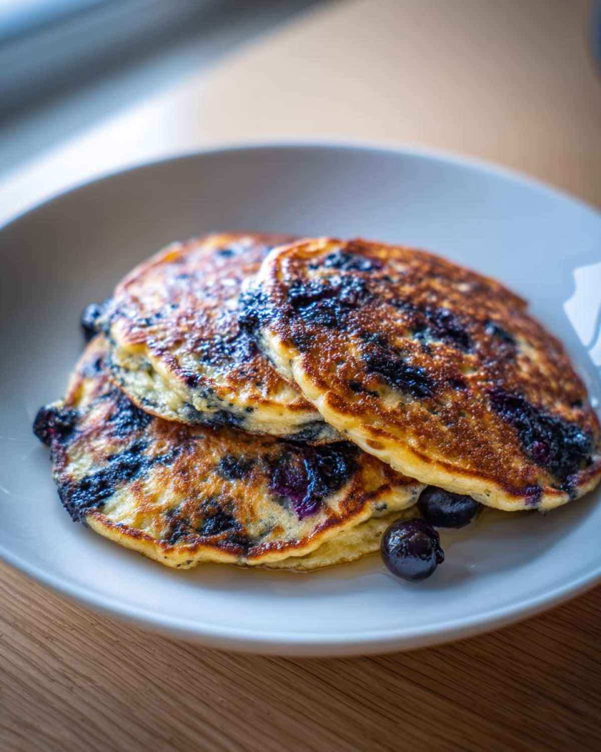 A stack of three golden-brown Lemon blueberry cottage cheese pancakes topped with fresh blueberries.