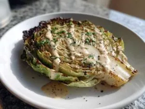 A thick, roasted lemon tahini cabbage steak drizzled with creamy sauce and sprinkled with herbs.