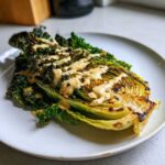 A grilled half-cabbage steak topped with crispy kale and drizzled generously with lemon tahini dressing.