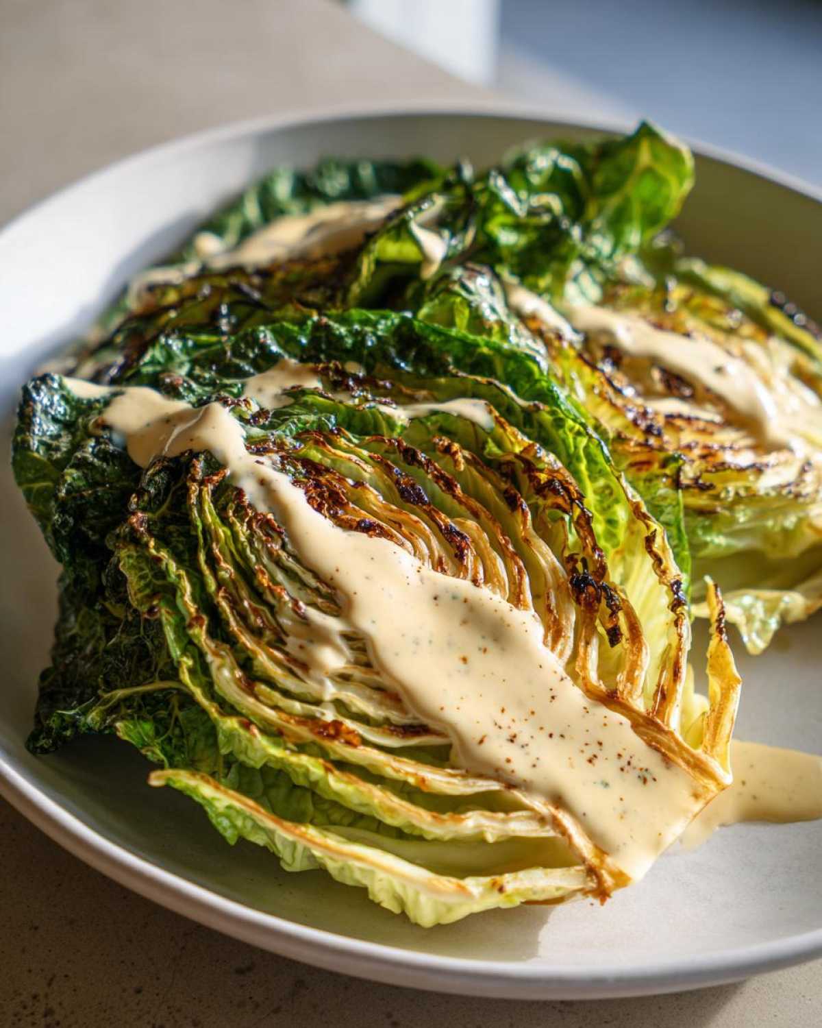 Close-up of grilled Lemon tahini cabbage steaks drizzled generously with a creamy tahini sauce.