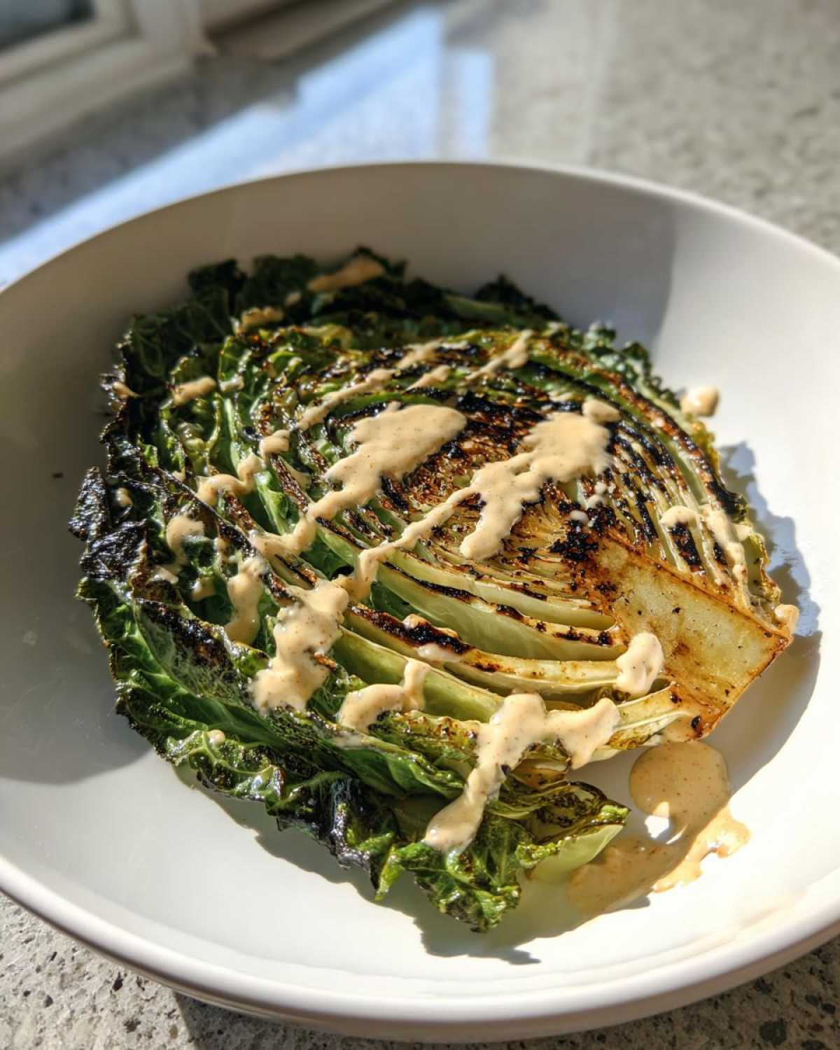 A grilled wedge of cabbage, served as a steak, drizzled generously with lemon tahini sauce.