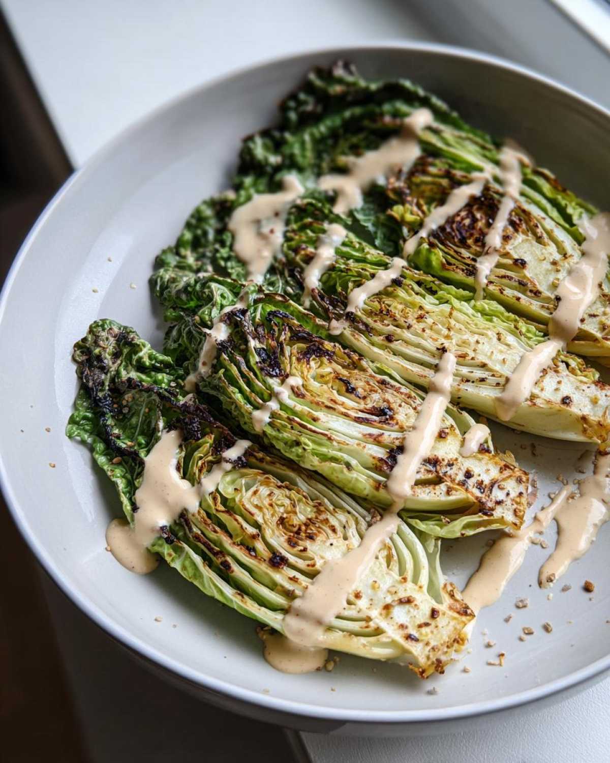 Close-up of grilled Lemon tahini cabbage steaks served on a plate and drizzled generously with tahini sauce.