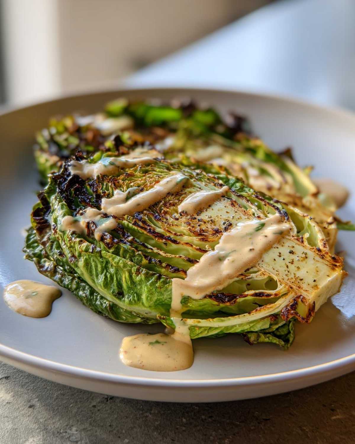 Two grilled Lemon tahini cabbage steaks drizzled generously with creamy tahini sauce on a light plate.