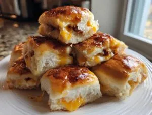 A stack of freshly baked mini grilled cheese Hawaiian rolls piled on a white plate, showing gooey melted cheese inside.