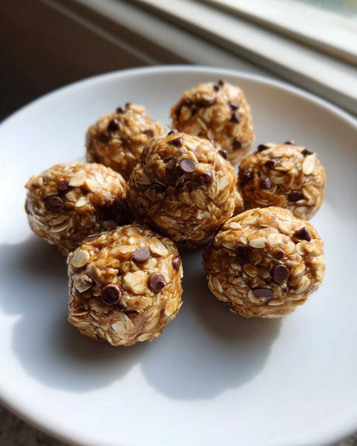 Seven homemade Peanut Butter Oatmeal Energy Bites studded with mini chocolate chips, arranged on a white plate.