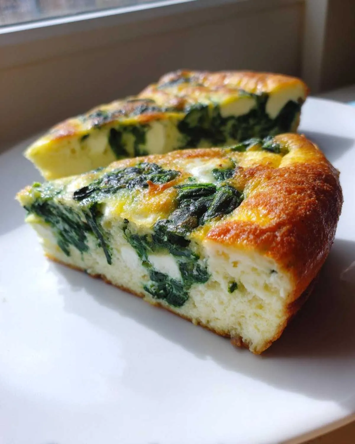 Two thick slices of baked ricotta and spinach frittata showing a golden crust and green spinach filling.