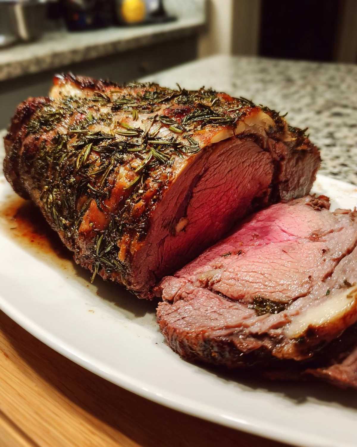 A succulent, medium-rare roast leg of lamb seasoned heavily with rosemary, partially sliced on a white platter.