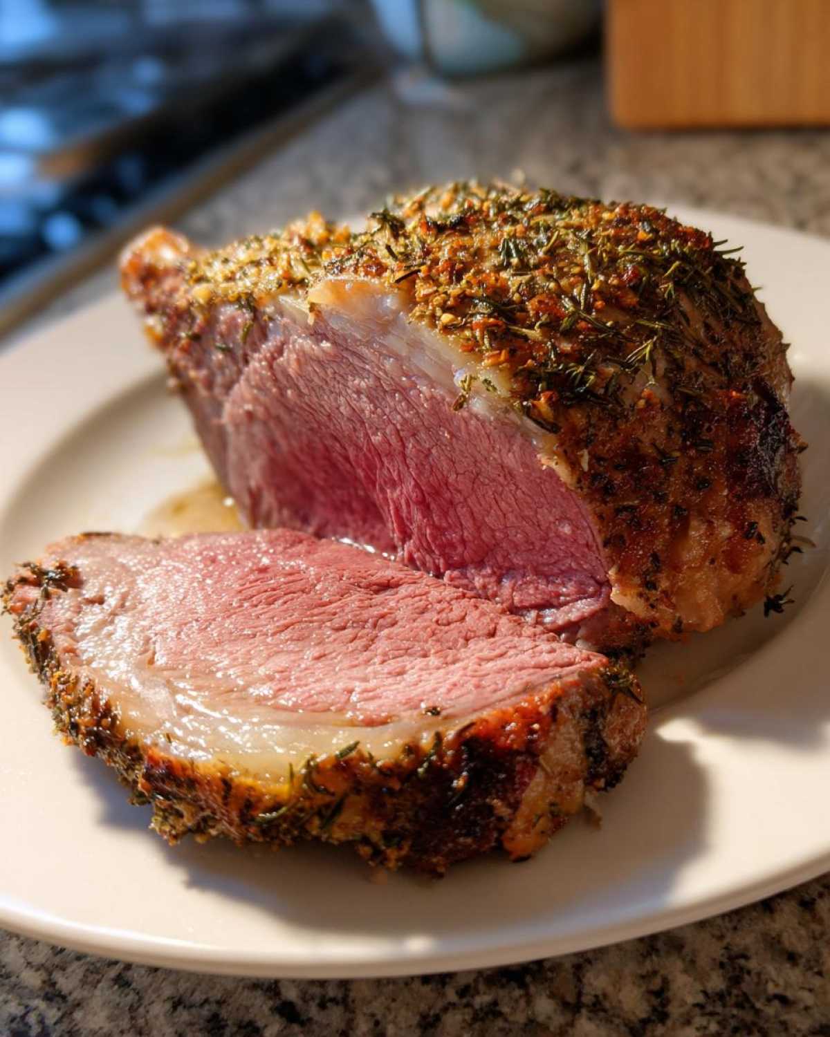 A thick slice of medium-rare roast leg of lamb with a flavorful herb crust, resting on a white plate.