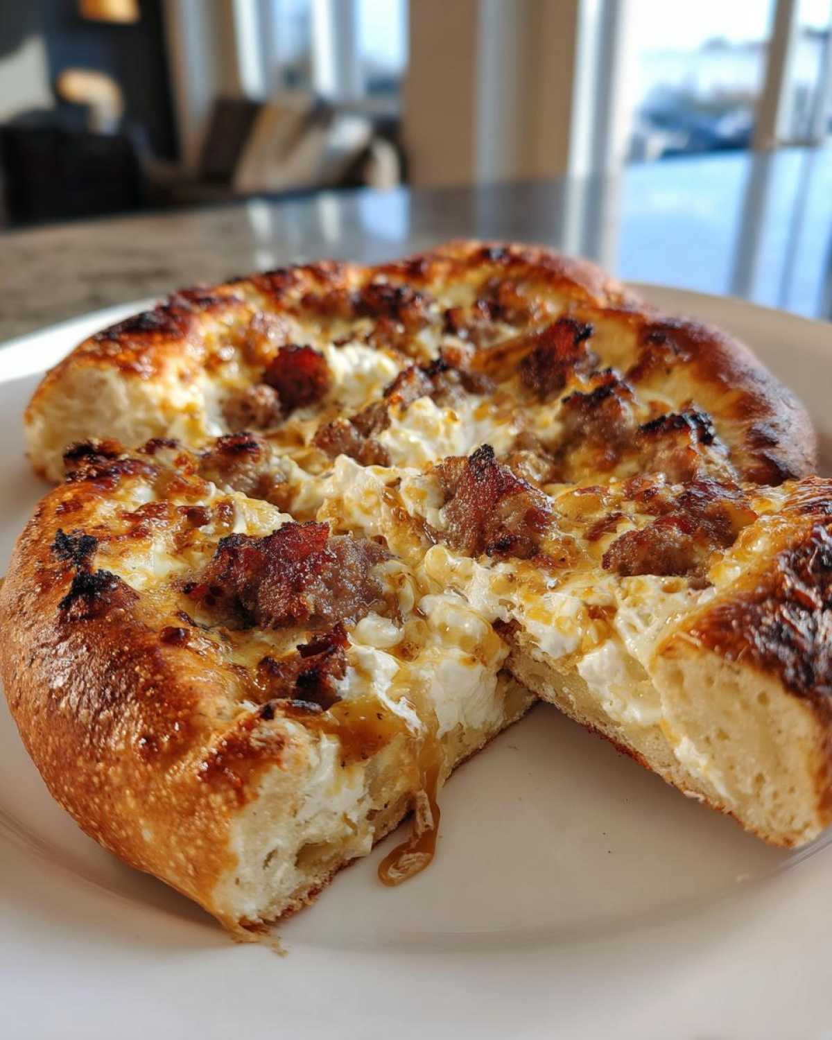 A close-up of a freshly baked sausage ricotta honey pizza, cut in half, showing the thick crust and dripping honey.
