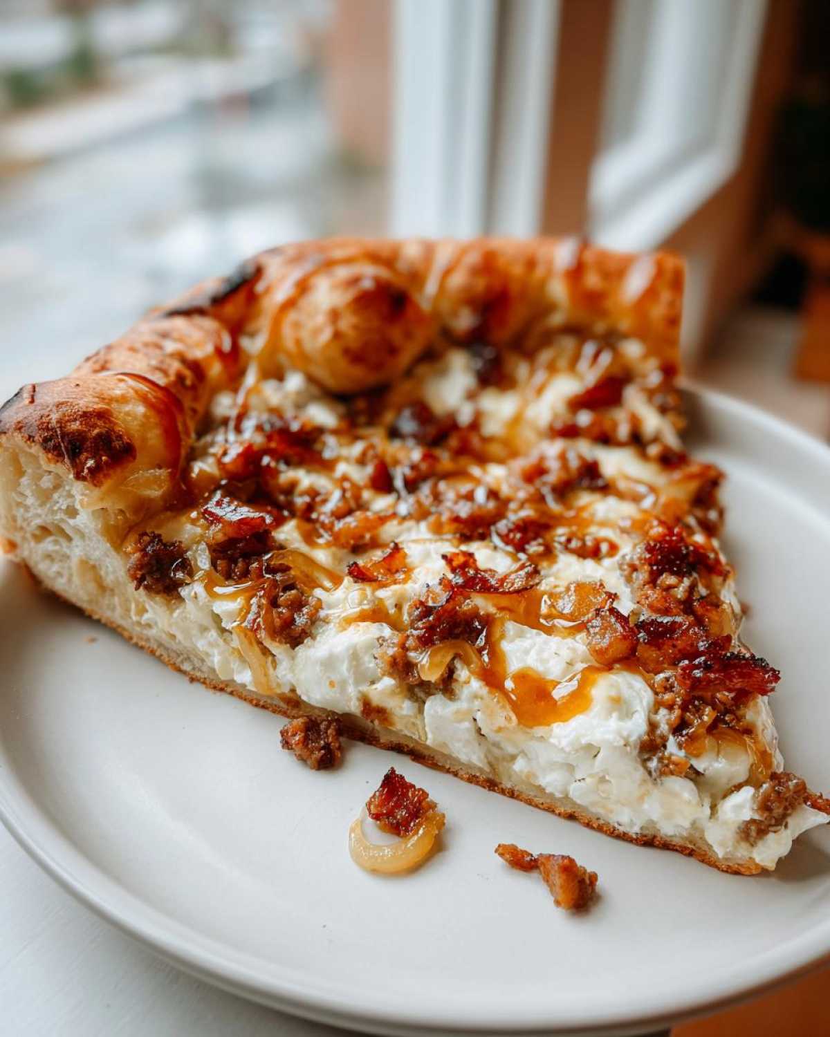 A thick slice of sausage ricotta honey pizza featuring a creamy white ricotta base, crumbled sausage, and a drizzle of honey.